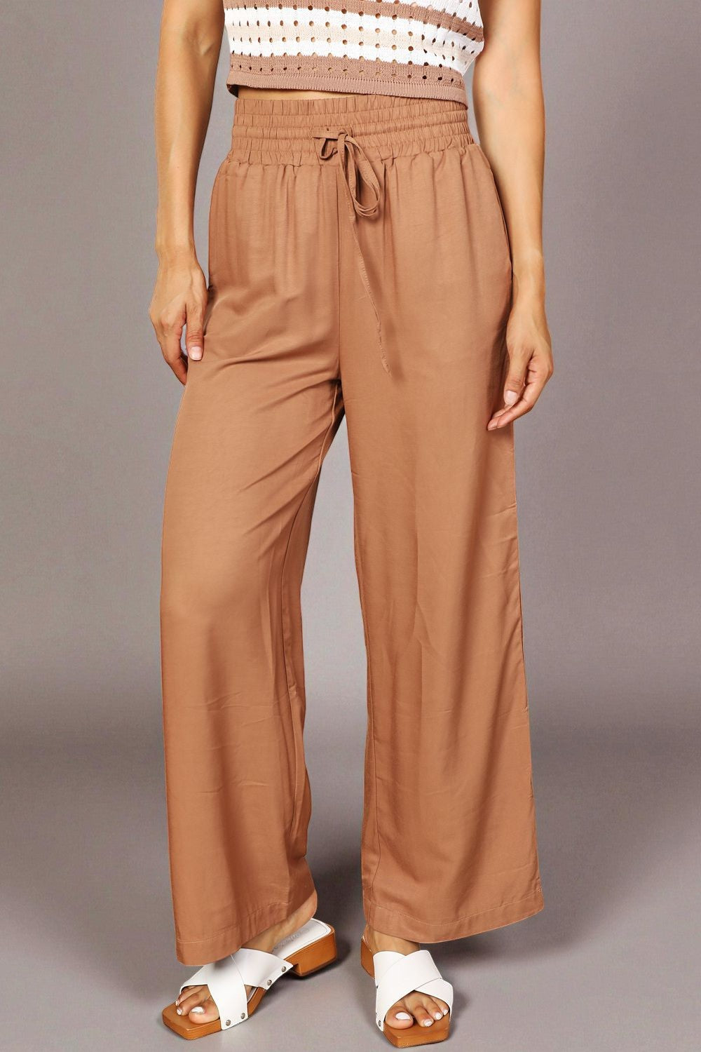 Person wearing brown wide-leg pants with a plain background
