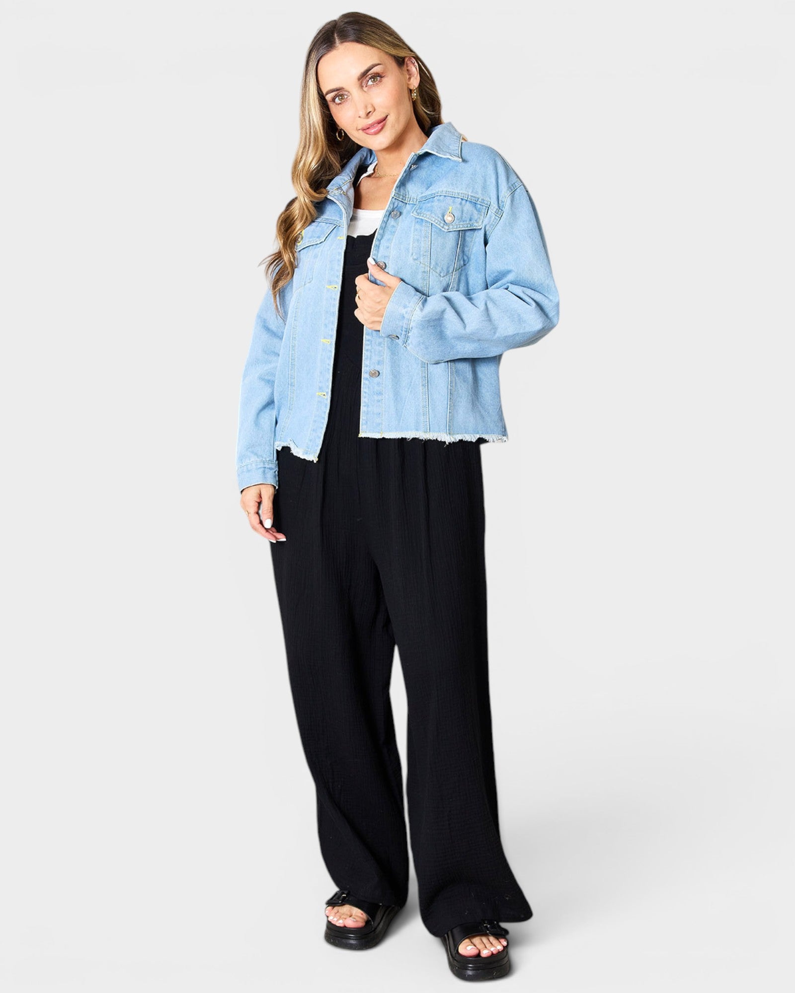 Woman wearing a light blue denim jacket over a black outfit on a white background