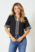 Woman wearing a black blouse with white patterns and blue jeans on a white background