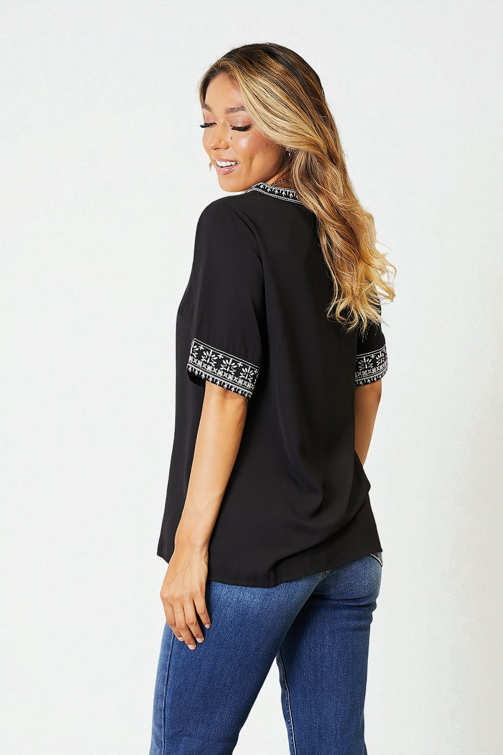 Woman wearing a black top with white patterns on sleeves against a white background