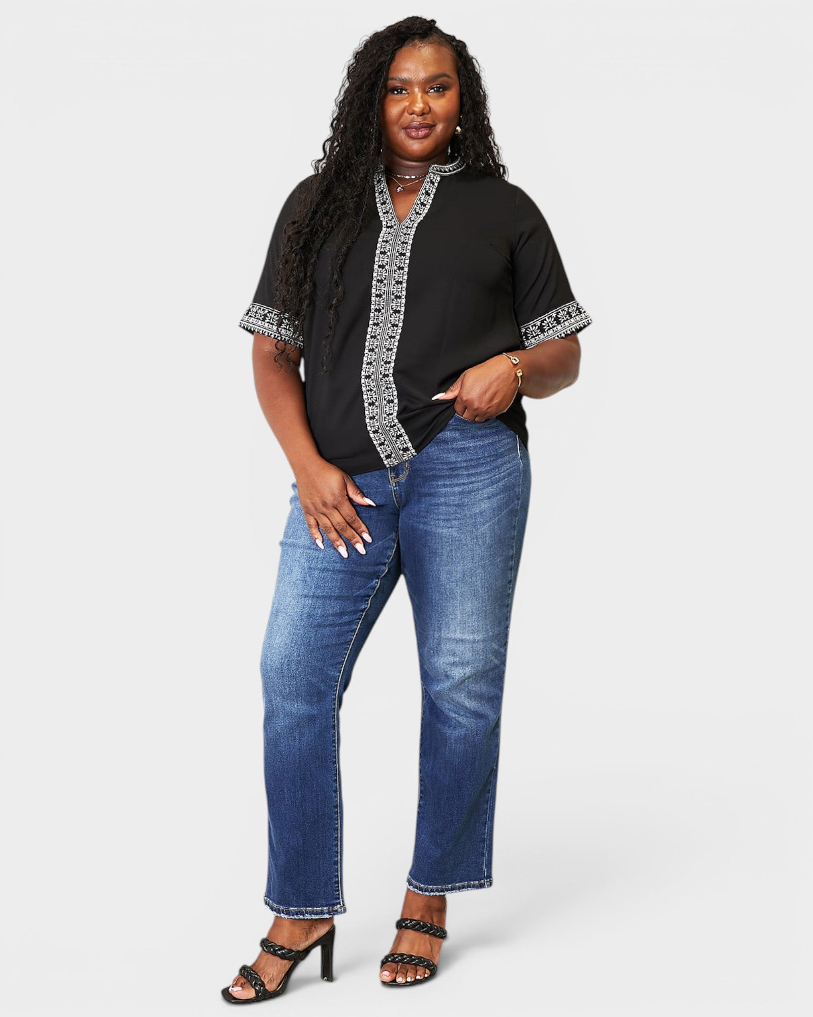 Woman wearing a black top with silver trim and blue jeans on a white background