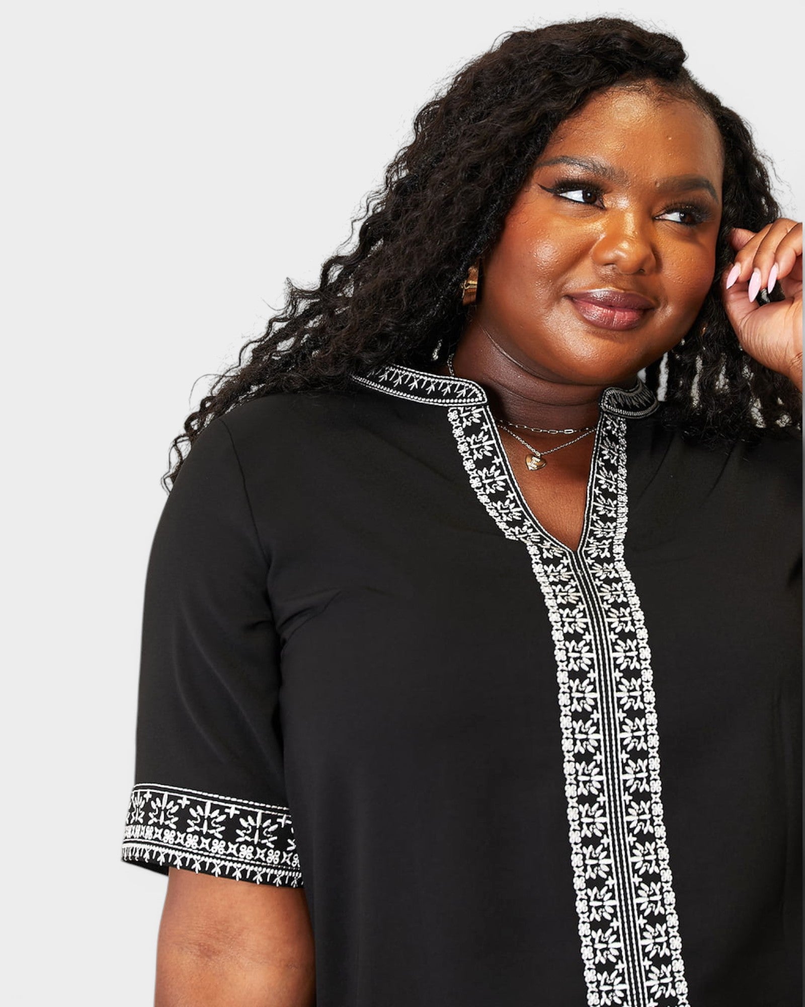Woman wearing a black top with white embroidery on a plain background