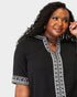 Woman wearing a black top with white embroidery on a plain background