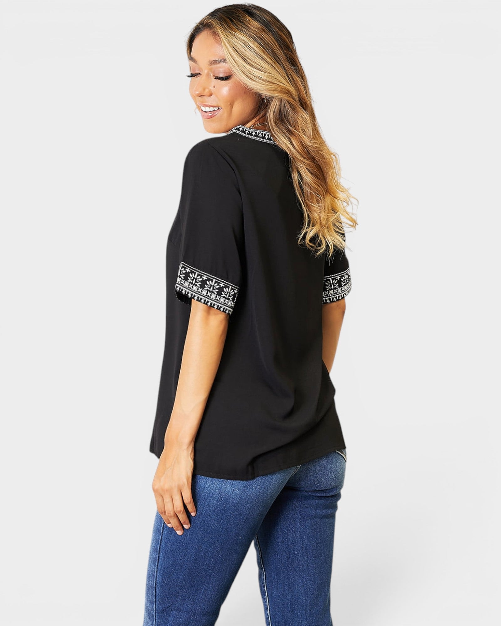 Woman wearing a black top with white patterned sleeves and blue jeans on a white background