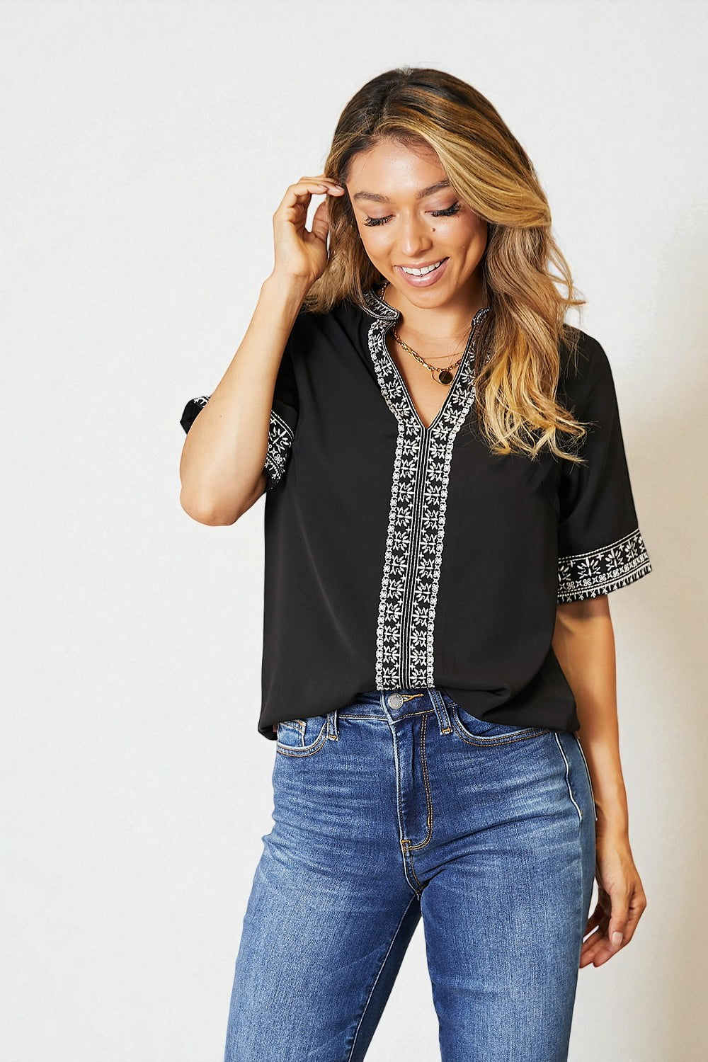 Woman wearing a black blouse with white embroidery and blue jeans on a plain background