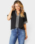Woman wearing a black top with white embroidery and blue jeans on a white background