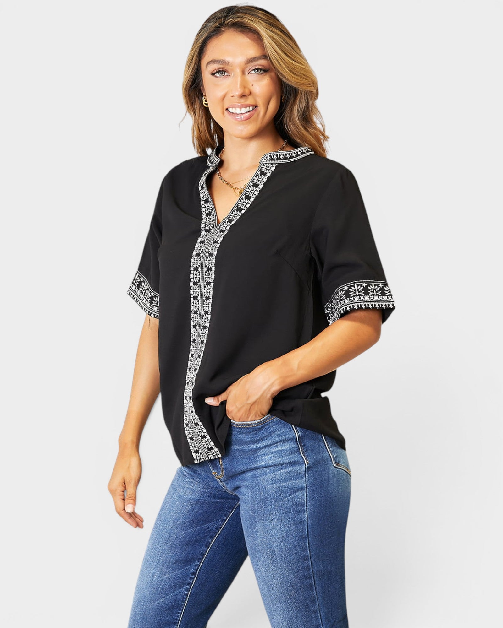Woman wearing a black blouse with white patterns and blue jeans on a white background