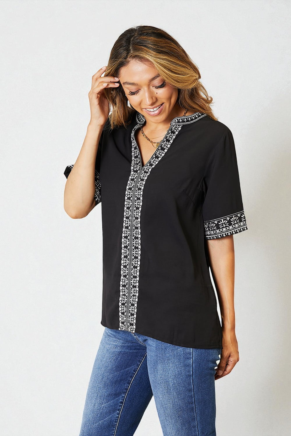 Woman wearing a black blouse with white embroidery on a plain background