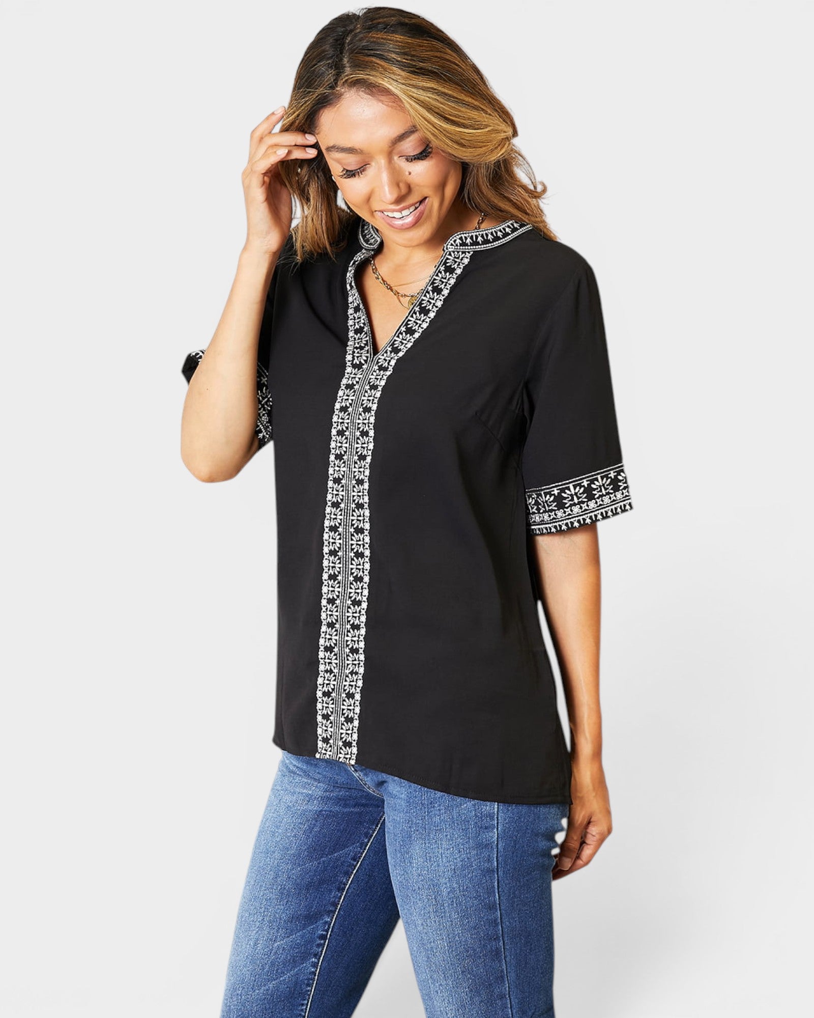 Woman wearing a black blouse with white embroidery and blue jeans on a white background