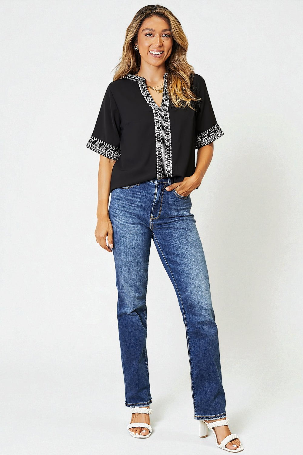 Woman wearing a black top with white trim and blue jeans on a white background