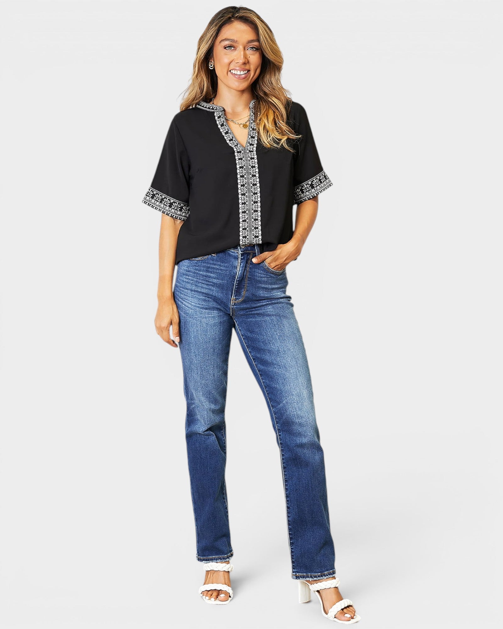 Woman wearing a black top with lace trim and blue jeans on a white background