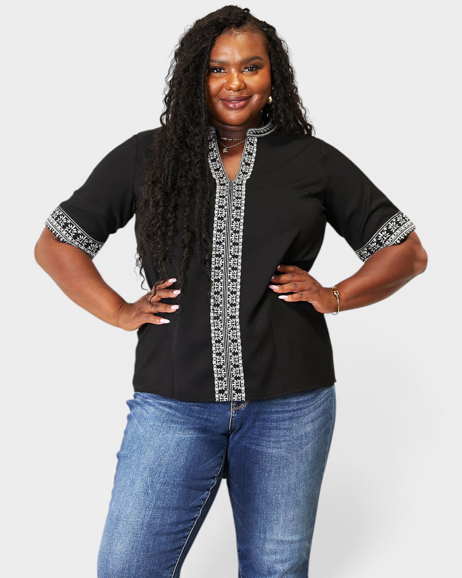 Woman wearing a black top with white patterns and blue jeans on a white background