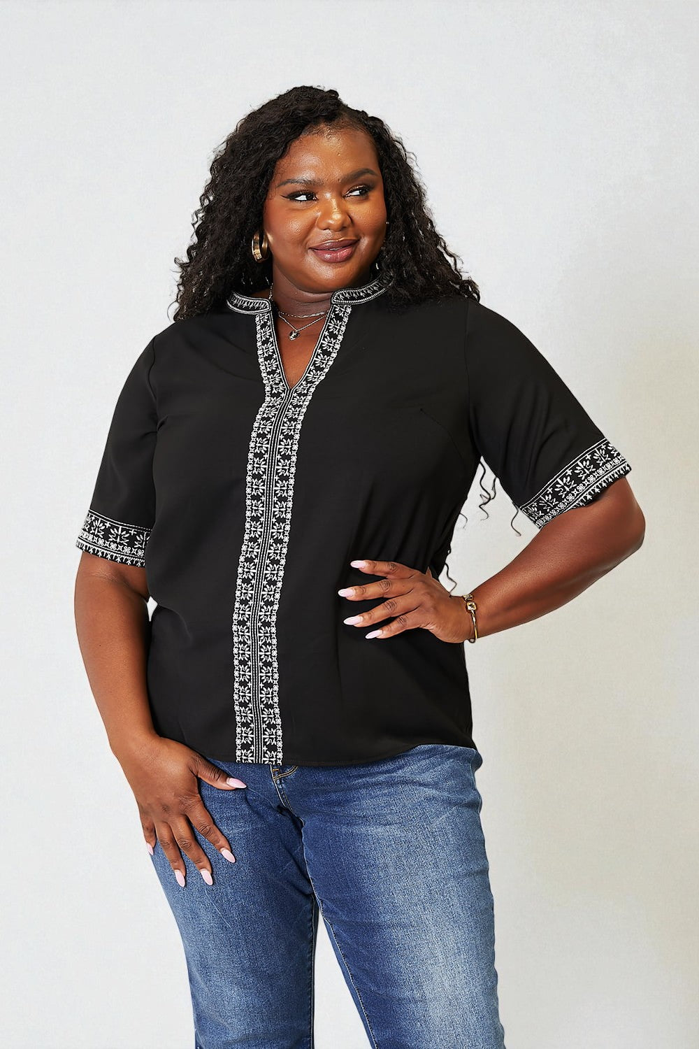 Woman wearing a black blouse with white patterns and blue jeans on a plain background