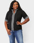 Woman wearing a black blouse with white embroidery and blue jeans on a light gray background
