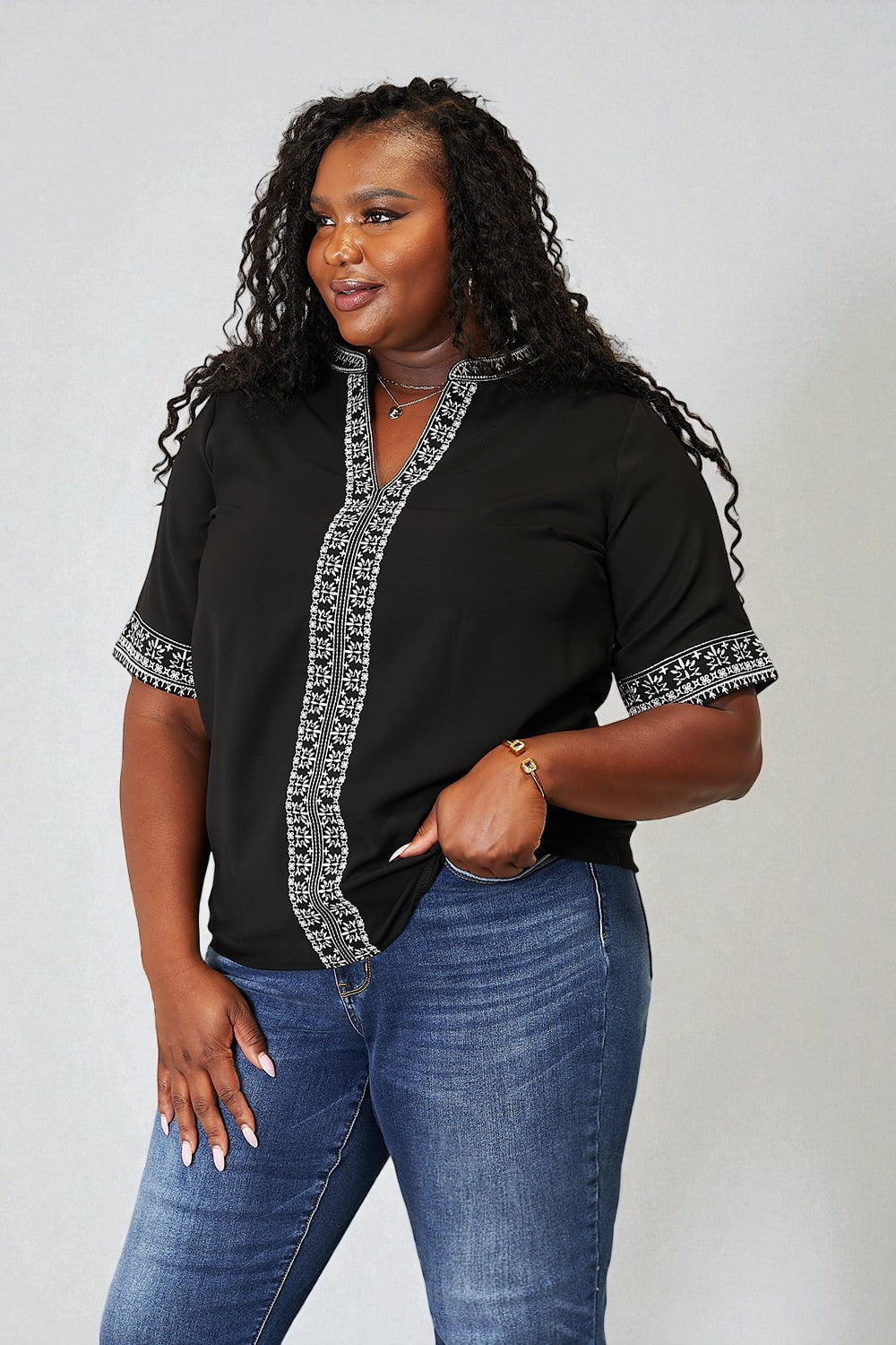 Woman wearing a black top with silver trim and blue jeans on a plain background