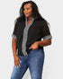Woman wearing a black top with white embroidery and blue jeans on a light gray background