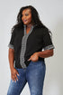Woman wearing a black top with silver trim and blue jeans on a plain background