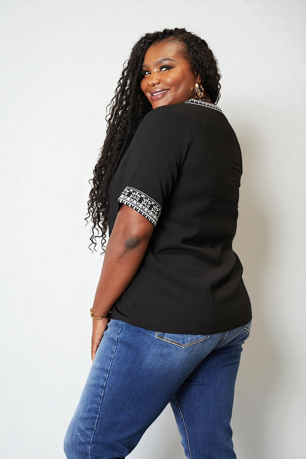 Woman wearing a black top with white patterned sleeves and blue jeans against a white background