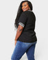 Woman wearing a black top with white patterned sleeves and blue jeans on a white background