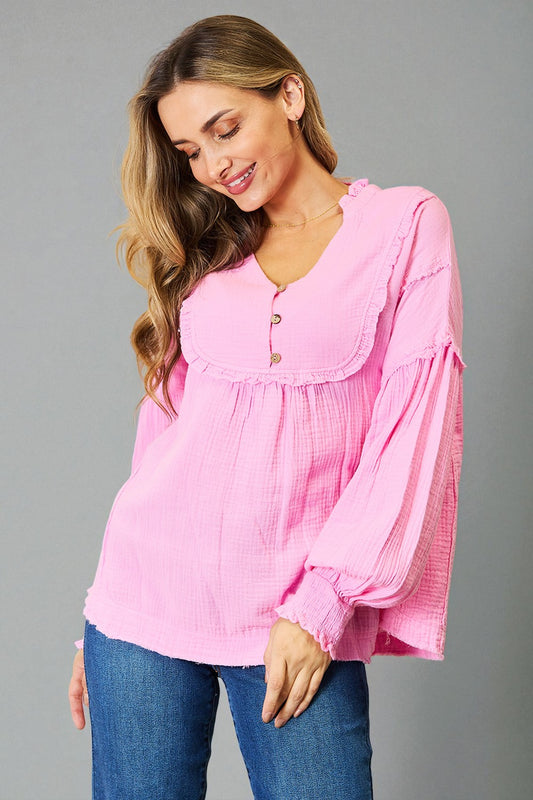 Woman wearing a pink blouse with long sleeves and blue jeans on a gray background