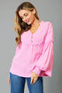 Woman wearing a pink blouse with long sleeves and blue jeans on a gray background
