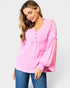 Woman wearing a pink blouse with long sleeves and blue jeans on a white background