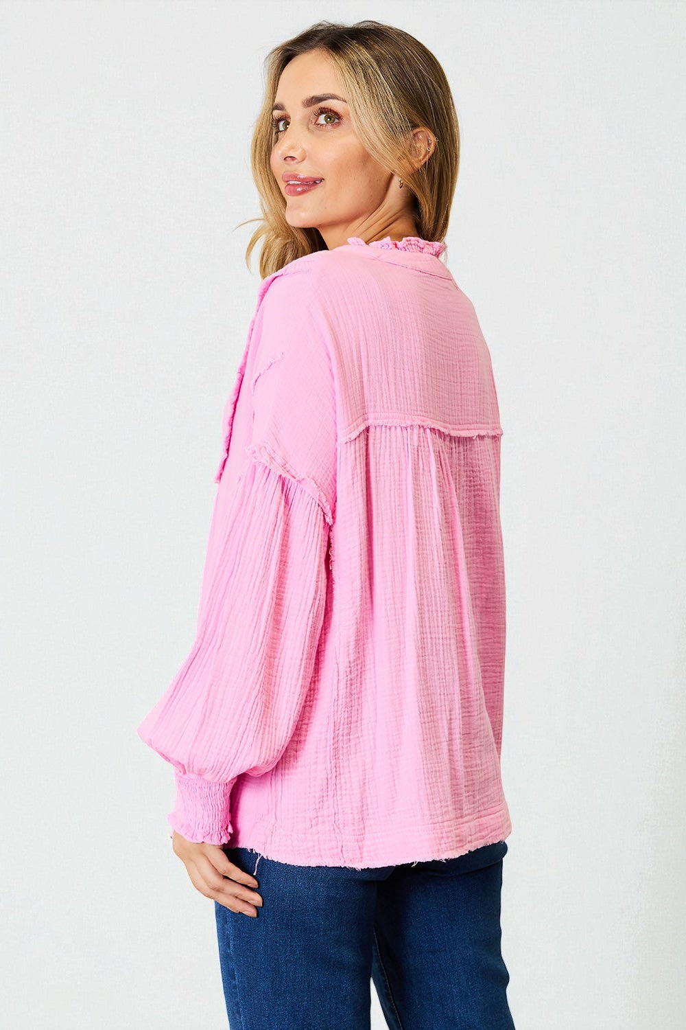 Woman wearing a pink textured blouse with blue jeans on a white background