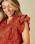 Woman wearing a red floral blouse with ruffled sleeves on a beige background