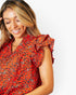 A woman wearing a red and orange floral print blouse with ruffled cap sleeves, shown in a close-up shot against a plain white background.