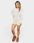 Woman wearing a white outfit with brown shoes on a plain background