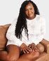 Woman sitting on a brown couch wearing a white long-sleeve shirt against a plain background