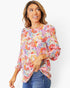 A woman wearing a colorful, long-sleeved floral print blouse with blue jeans, photographed against a clean white studio background.