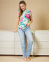 Woman wearing a floral sleeveless top and jeans against a beige wall.
