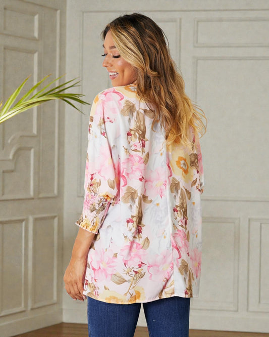 Woman wearing a floral kimono-style top in a room with decorative paneling.