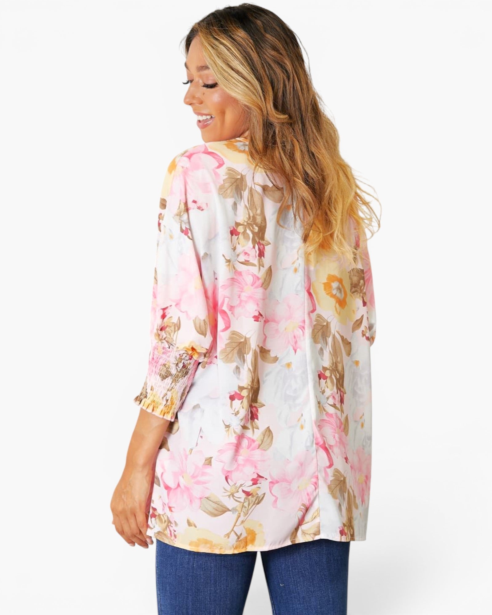 A woman shown from the back wearing a white three-quarter sleeve blouse with a pink and gold floral print, paired with blue jeans, against a plain white background.