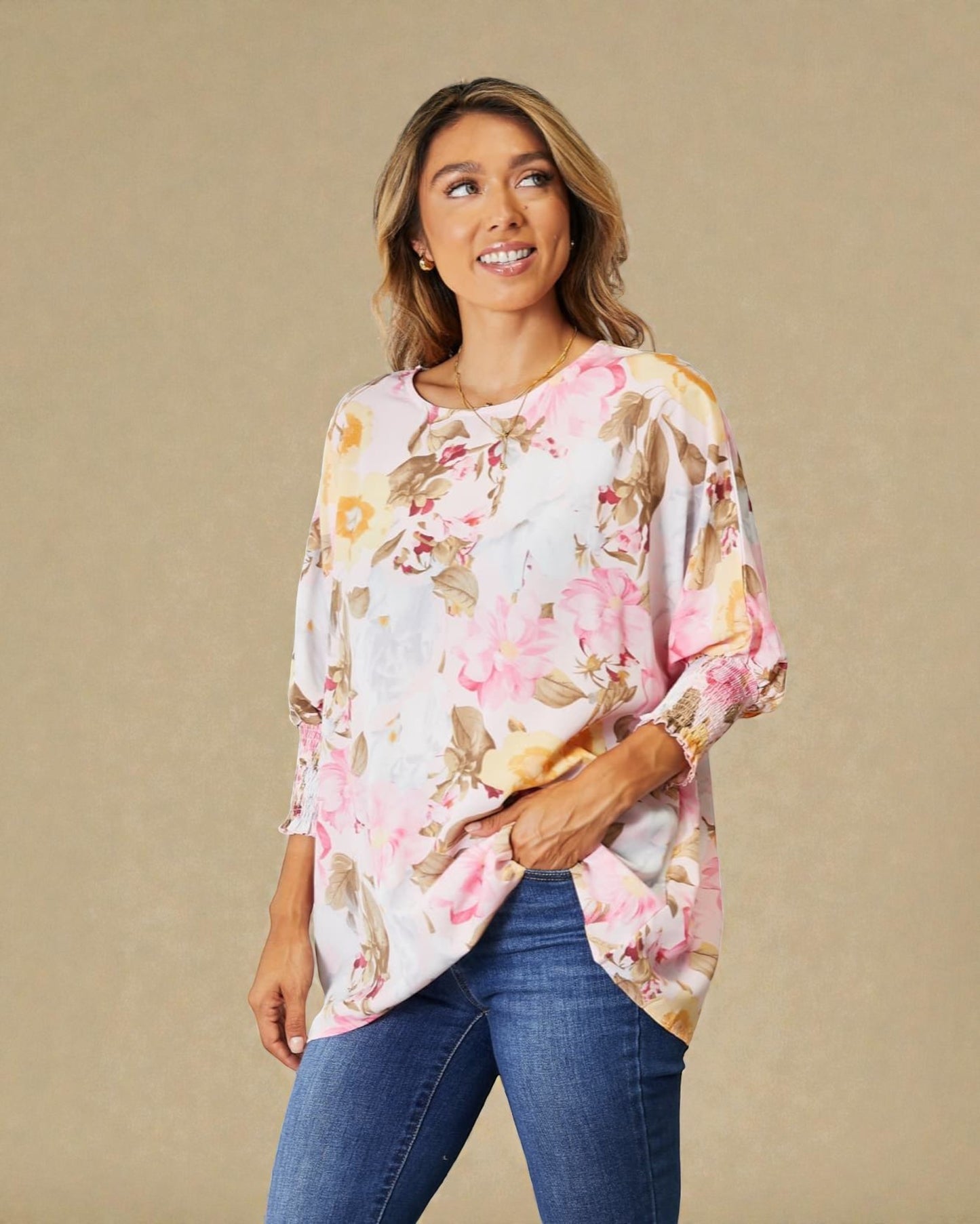 Woman wearing a floral blouse and jeans against a beige background