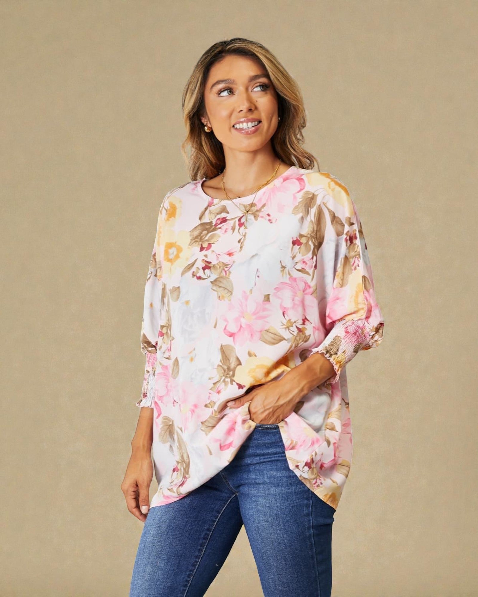 Woman wearing a floral blouse and jeans against a beige background