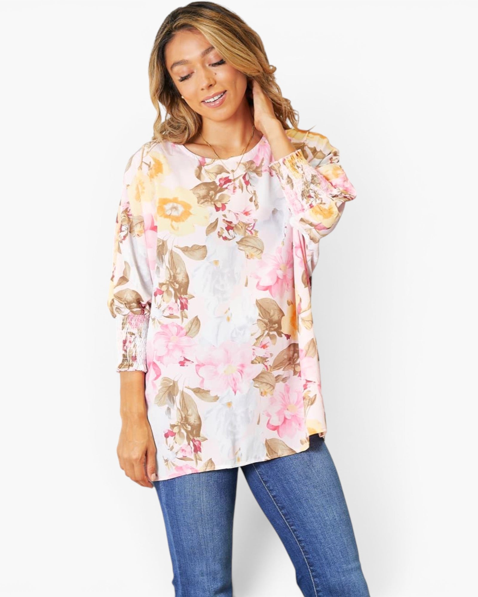 A woman wearing a white long-sleeve tunic top with a pink, yellow, and brown floral print, paired with blue jeans, against a plain white background.