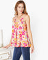 A woman wearing a colorful floral print camisole top with thin straps and blue jeans, standing next to a white dresser in a bright room.