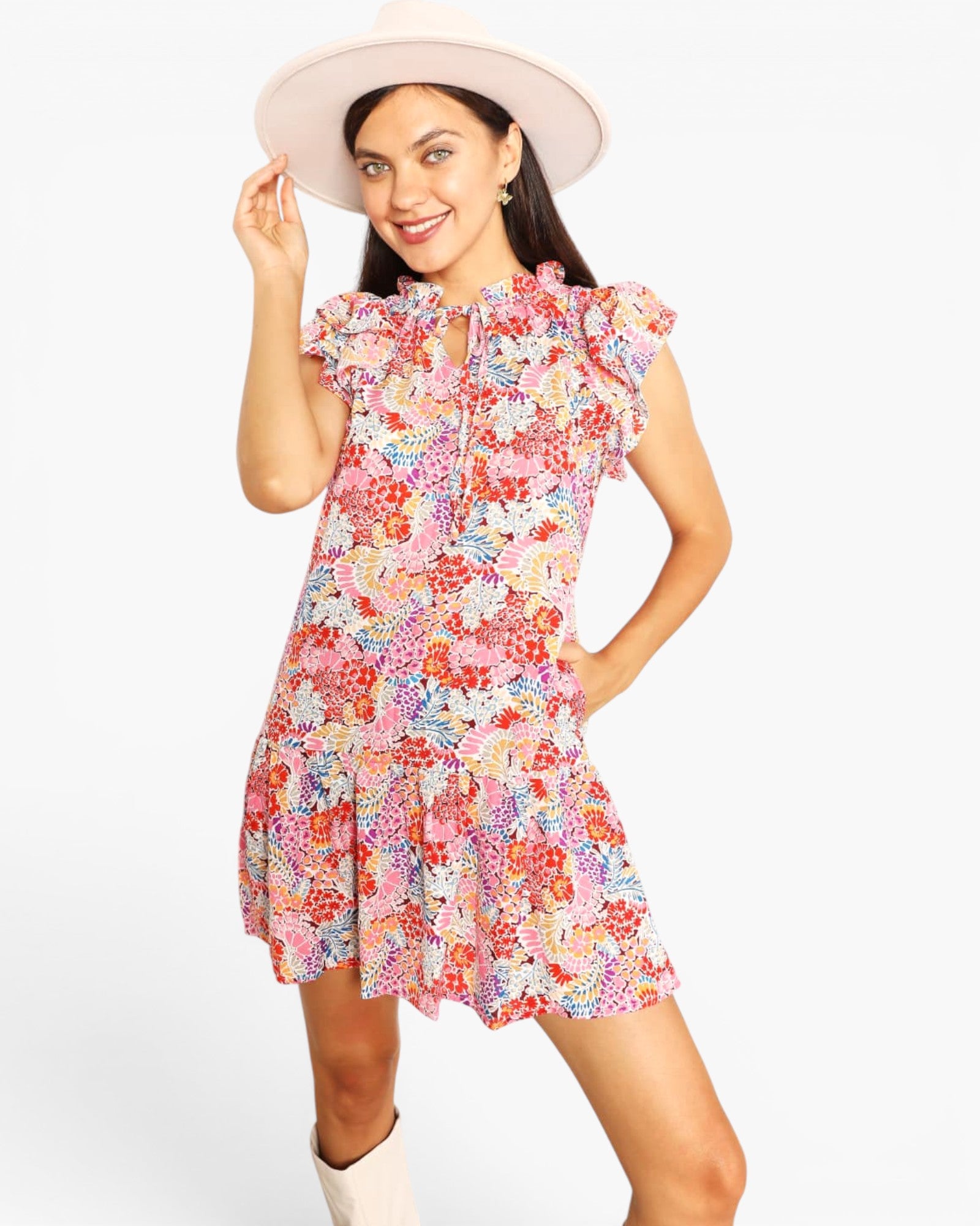 A woman modeling a short pink floral dress with ruffled cap sleeves and a front zipper, paired with a wide-brimmed light pink hat and white boots, against a plain white background.