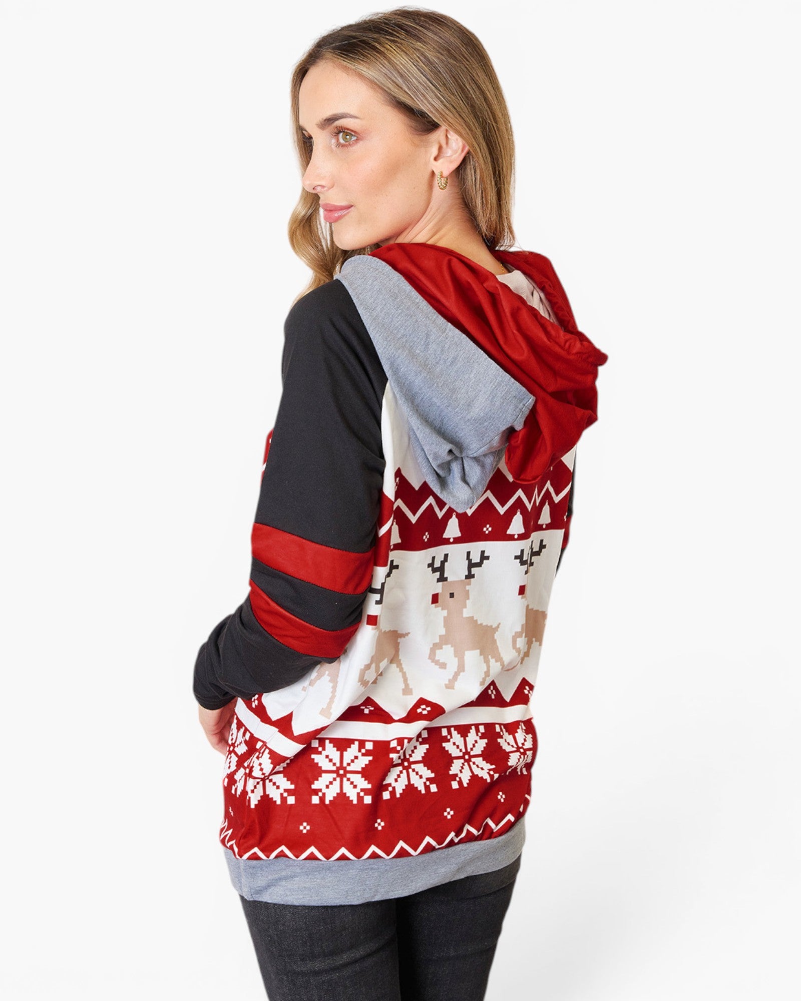 A woman wearing a holiday-themed raglan hoodie, shown from a three-quarter back view. The hoodie features a red hood and upper sleeve, a black lower sleeve, and a white body decorated with a red Nordic snowflake pattern and beige reindeer motifs.