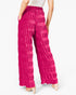 A person wearing bright pink wide-leg pleated pants with a textured, crinkled fabric, shown from the back against a plain white background.