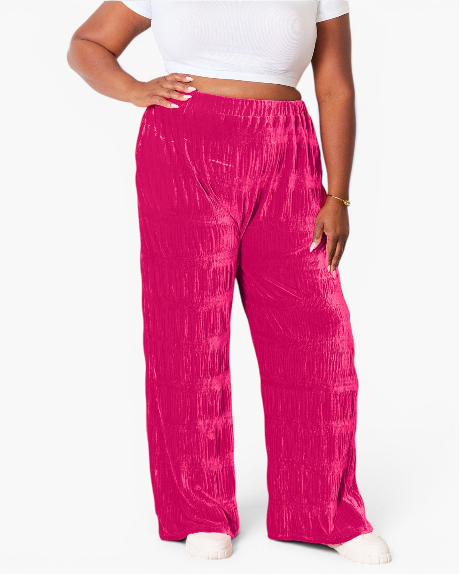 A person wearing bright fuchsia pink wide-leg pants with a crinkled texture, paired with a white crop top and white shoes, shown against a plain white studio background.