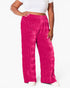 A person wearing bright fuchsia pink wide-leg pants with a crinkled texture, paired with a white crop top and white shoes, shown against a plain white studio background.