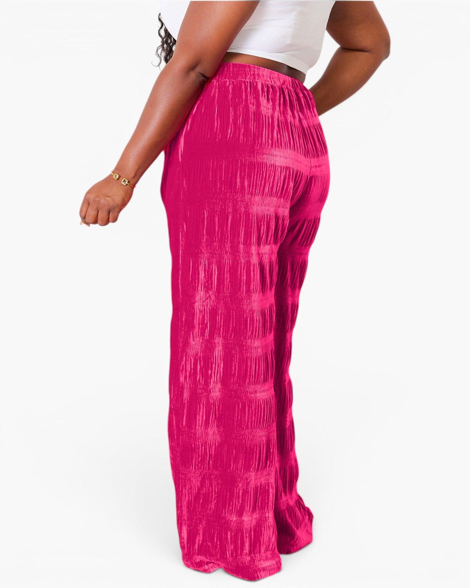 A person wearing bright pink pleated wide-leg pants with a white cropped top, shown from the back against a plain white studio background.