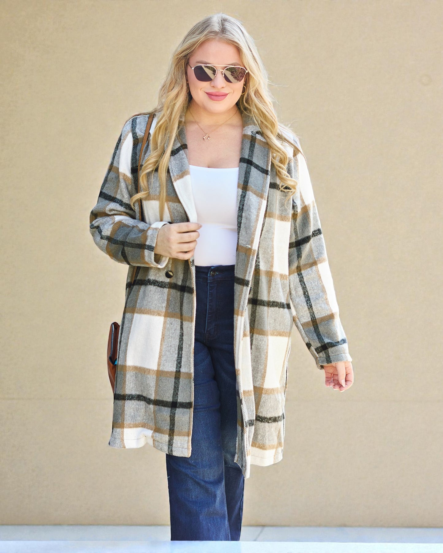 Woman wearing a plaid cardigan over a white top and blue jeans against a beige background