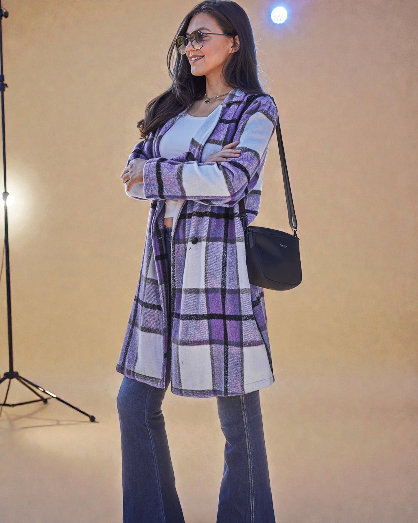 Woman wearing a plaid coat and sunglasses, standing against a plain background