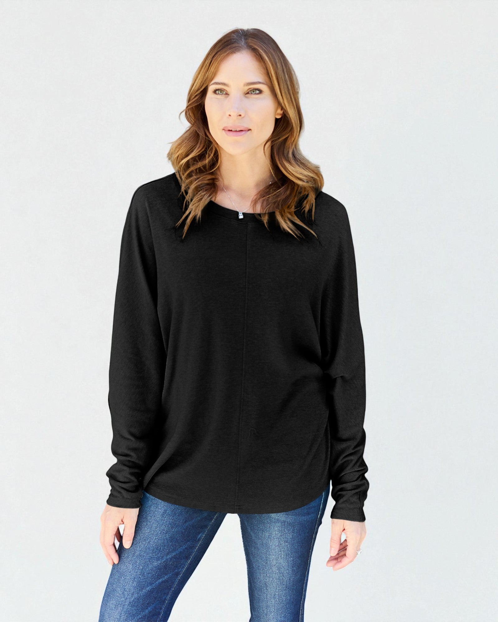 Woman wearing a black long-sleeve top and blue jeans against a plain background