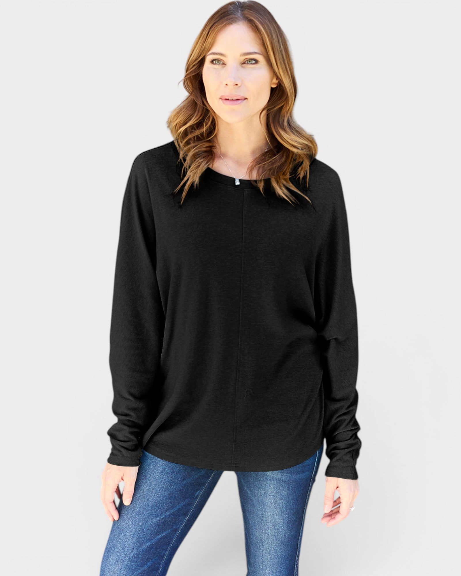 Woman wearing a black long-sleeve top and blue jeans on a gray background