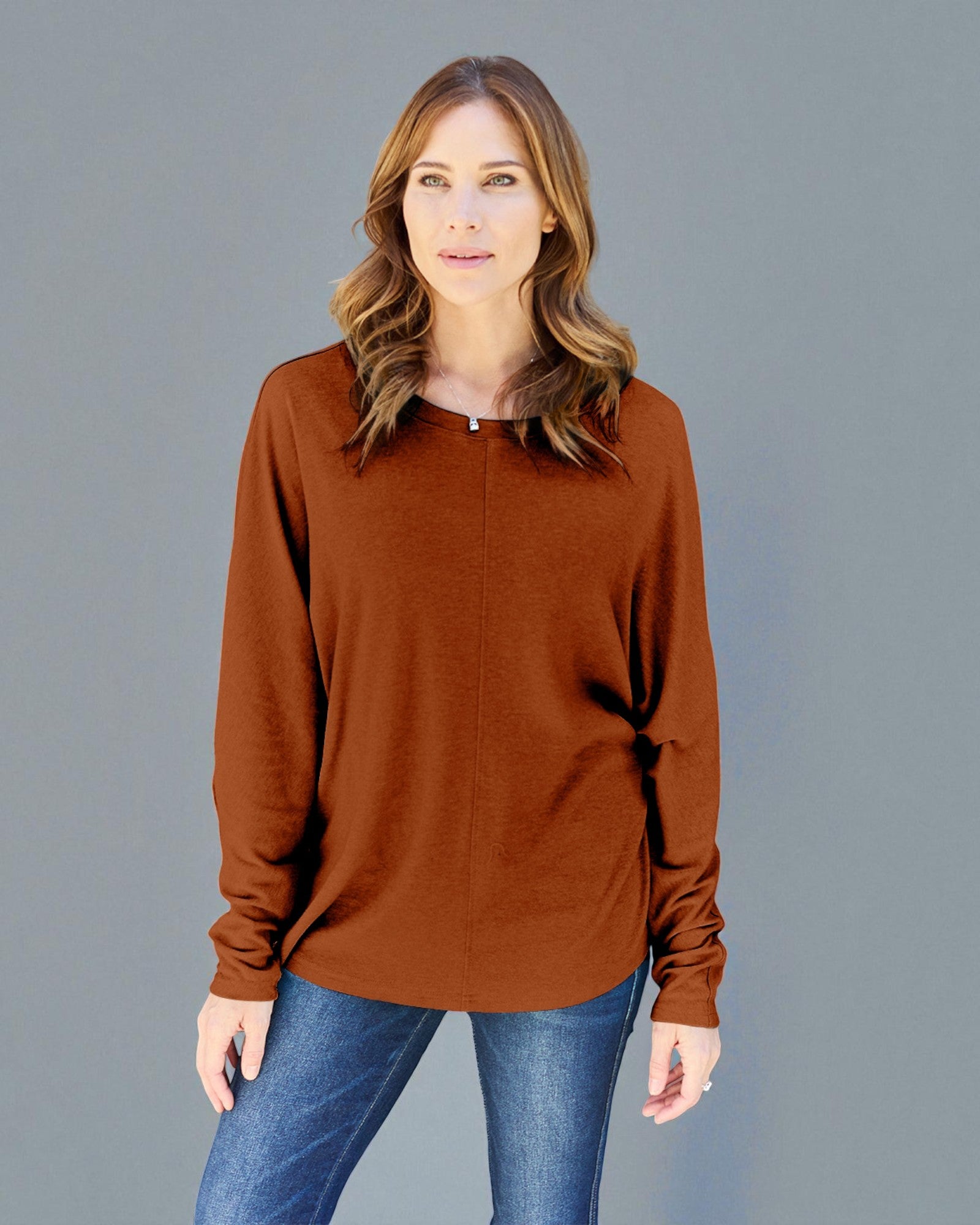 Woman wearing a brown long-sleeve top and blue jeans against a gray background